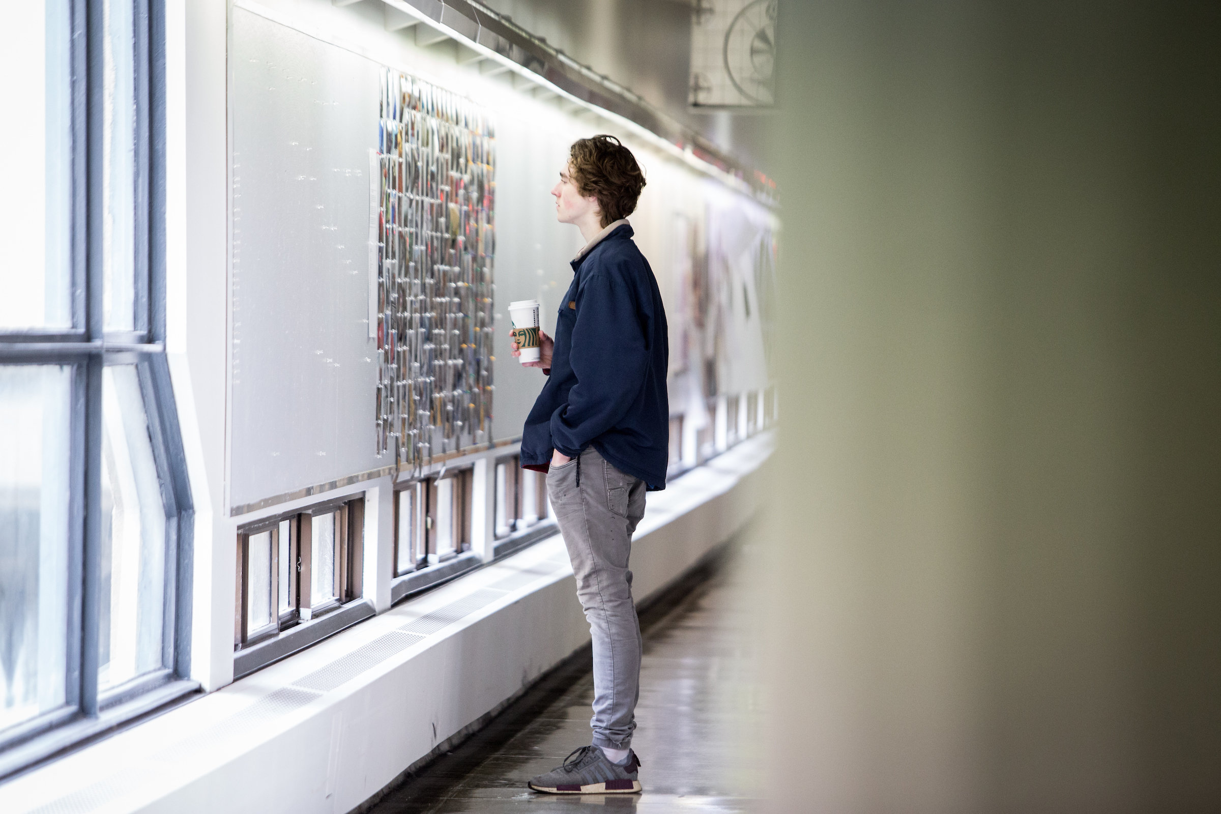Photo of a VAC student looking at photography artwork in the Humanities building 6th Floor hallway. 