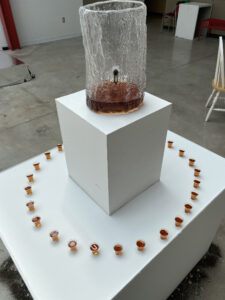 Iskigamizigan (Sugarbush), 2023, mold blown glass, maple syrup, dirt, metal antique tap, communion cups by Abby Sunde, BFA 2024