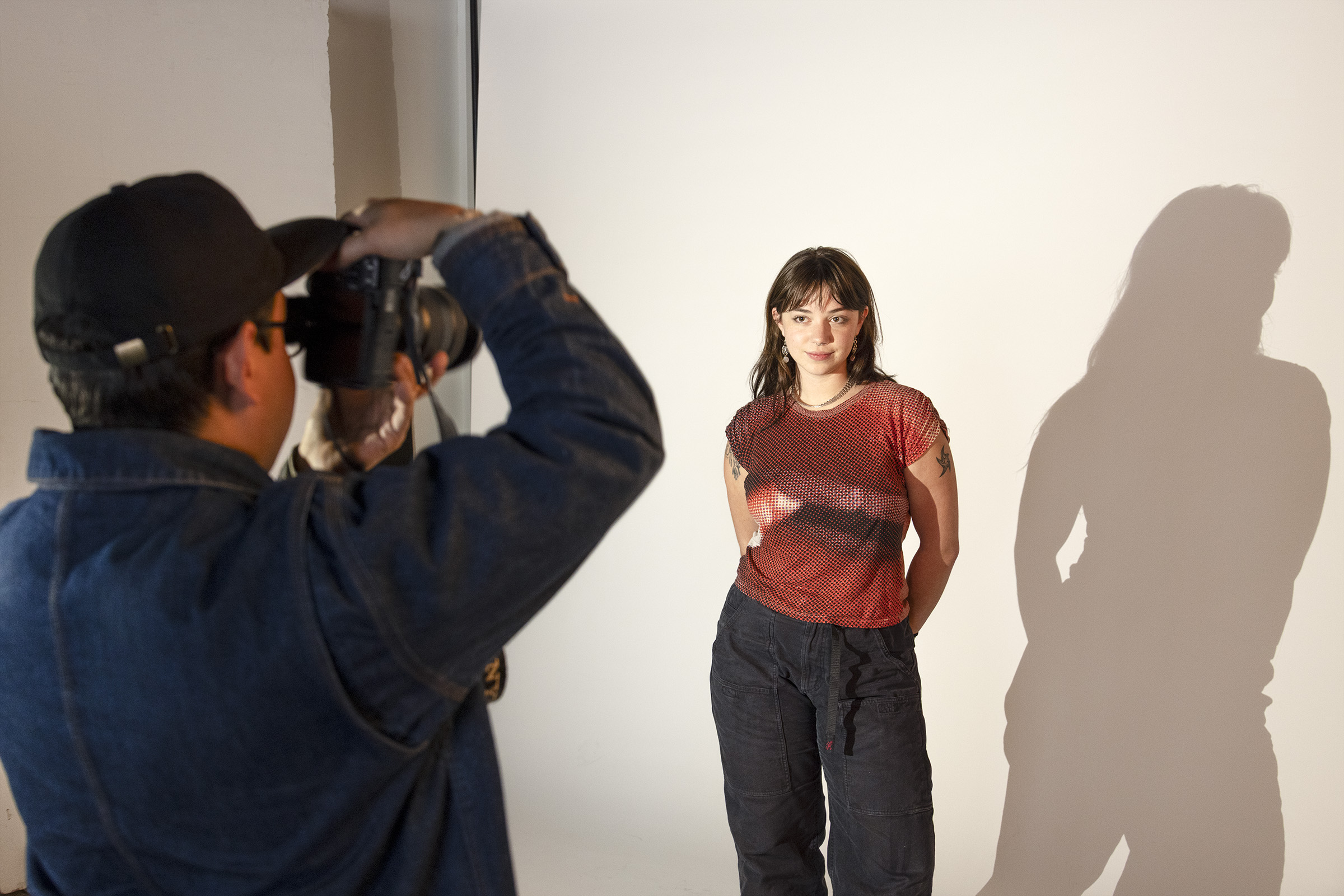 A person poses against a blank backdrop as a student photographs them in the Lighting Studio at the University of Wisconsin–Madison.